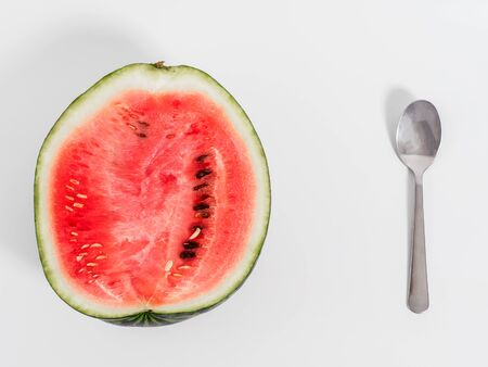 Spoon with halved watermelon with silver on white background. Isolated part of watermelon with yellow spot on the side. Top view and copyspace for text.の写真素材