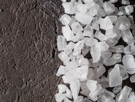 Crystals of sea salt on dark background. Closeup view of important food mineral.