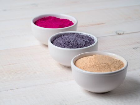 Set of superfoods in white bowls on wooden background. Blue butterfly pea, lucuma and dragon fruit powder in the bowls. Copyspace for text.の写真素材