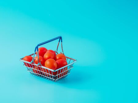 Shopping cart with tomatoes on blue background. Toy supermarket cart with fresh cherry. Copyspace for text.の写真素材