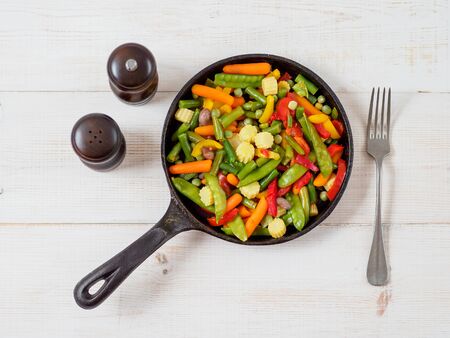 Fresh vegetables fried in the pan. White wooden background and space for text.の写真素材