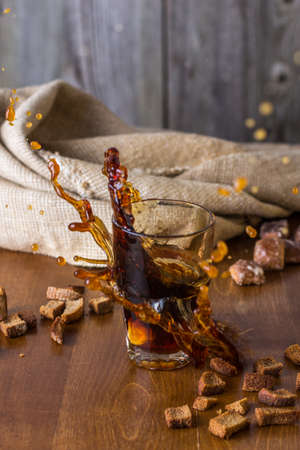 Traditional Russian drink kvass from bread, rye malt, sugar and water. Kvass in a glass on a dark wooden background. Splashの写真素材