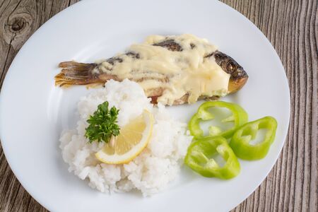 Fried crucian with garnish in a white plate on a wooden backgroundの写真素材