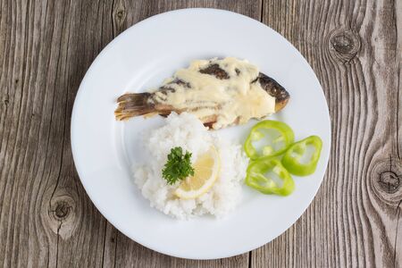 Fried crucian with garnish in a white plate on a wooden backgroundの写真素材