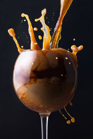 Splashes of coffee with milk in a glass on a black backgroundの写真素材