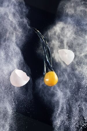 Still life - broken eggs flying between scattered flour