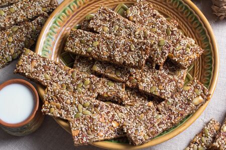 Kozinaki from sesame and peanuts seeds of sunflower and pumpkin and other nuts on a beautiful plate with a cup of milkの写真素材