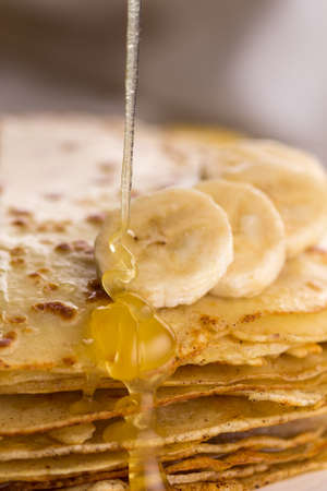 Thin pancakes with butter and honey on a white plate. Maslenitsa. Russian pancakes on a light wooden background. In a rustic style. Country style.の写真素材