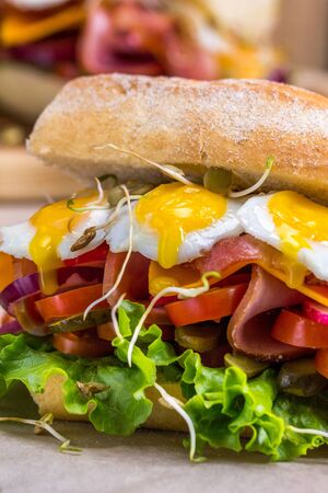 A sandwich with bacon, cheese and fried quail eggs. A sandwich with fresh vegetables and herbs on a wooden background. Rustic.の写真素材