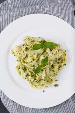 Homemade pasta from basil and arugula with green pesto in a white plate on a dark background. Italian Cuisineの写真素材