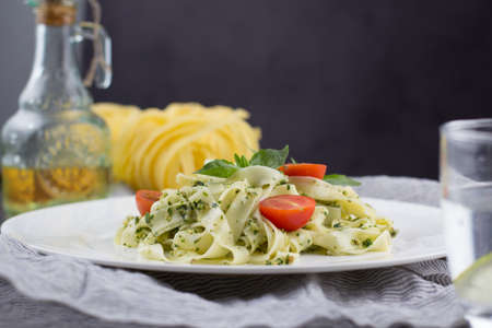 Still life - Homemade pasta from basil and arugula with green pesto in a white plate on a dark...