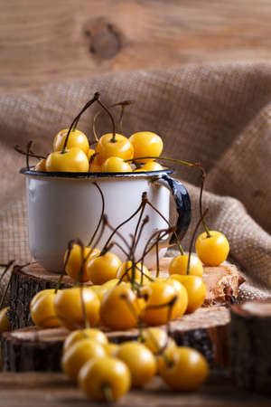 Yellow cherry in a rustic style on a wooden background. Berries of ripe fresh cherries in a cup.の写真素材