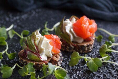Delicious canape with salmon, cottage cheese, olive with micro greens on a dark background. Cold appetizer on a black background.の写真素材