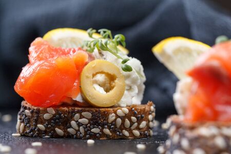 Canape with salmon and cheese cheese on a dark background. Fresh juicy cold.