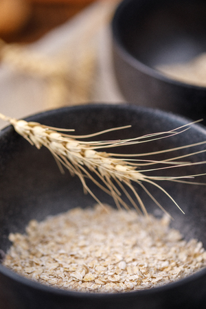 Still life. Dry flakes of oatmeal in a black refined bowl and spikelets.