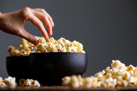 A cup full of popcorn and the hand that takes it. Still-life on a wooden background.の写真素材
