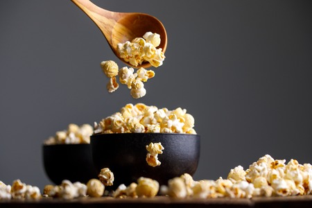 Popcorn falls from a wooden spoon into bowls and around them. Appetizing still life.の写真素材