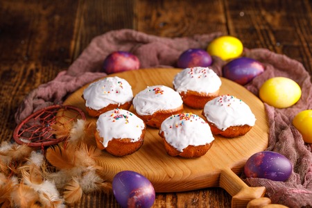 Cupcakes on a decorative board and unusually painted Easter eggs. Still-life on a wooden background.