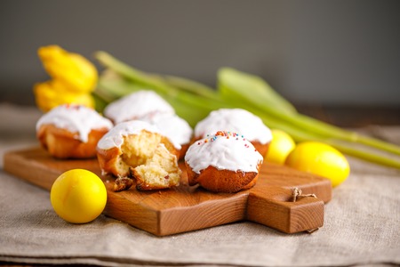 A gentle still-life with fresh pastries and Easter eggs painted in yellow with tulips in the background. Still life with textiles on a wooden background.の写真素材