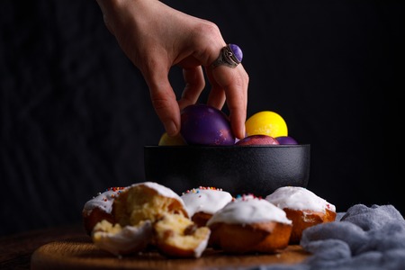 A hand with a delightful ring that takes an Easter egg of the same unusual color from a ceramic bowl. Close-up.の写真素材