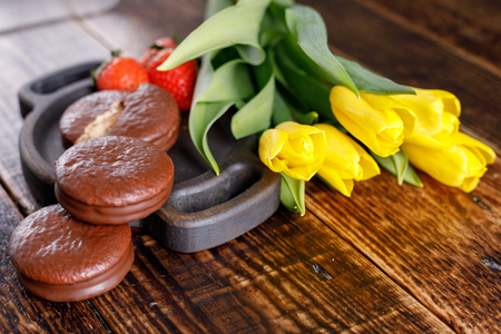 Strawberries, chocolate cookies and yellow tulips on a wooden background.の写真素材