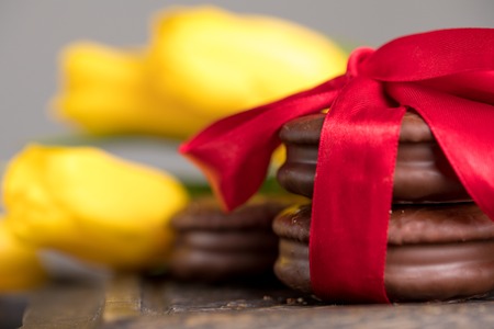 Chocolate biscuits, tied with satin red ribbon. Chocolate biscuits with a delicate filling and a tulip flower. A gift for Valentine's Day.の写真素材
