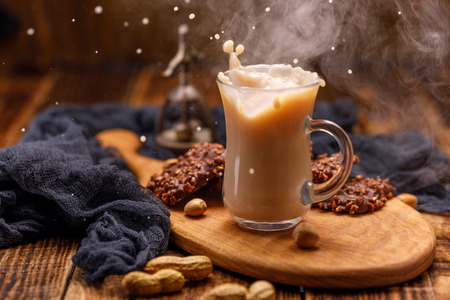 Smoking, tea with milk and chocolate biscuits with nuts for breakfast are spilled from the cup. Tea with biscuits in a glass cup with a splash.の写真素材