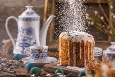 Easter decorations in a rustic style with a vintage set and an ancient frame. Sugar powder is poured onto the Easter cake. Still-life as a postcard to Easter.の写真素材