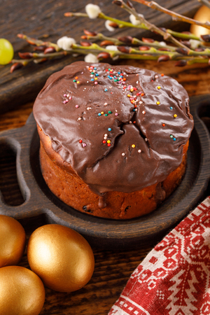 Delicious Easter home cake in chocolate glaze and traditional Easter eggs painted in golden color....