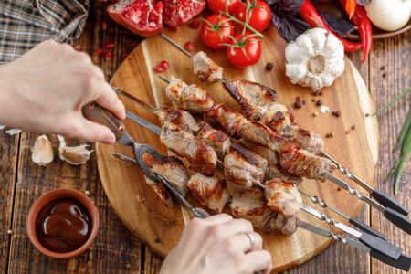 Rustic still life. Juicy pork meat is cut with a knife and fork. Appetizing shish kebabs and fresh vegetables on a wooden background. View from above.の写真素材