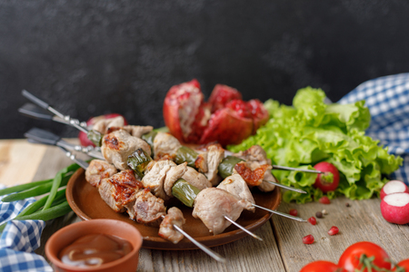 Shish kebabs on skewers laid out on a plate and fresh vegetables. Rustic. Still life on a wooden background with textiles. Close-up.の写真素材