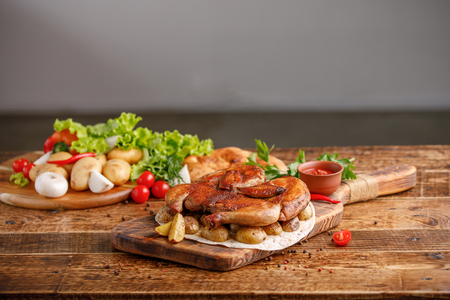 Fried chicken with garnish of baked young potatoes with fresh vegetables. Rustic. Appetizing still life on a wooden background.の写真素材