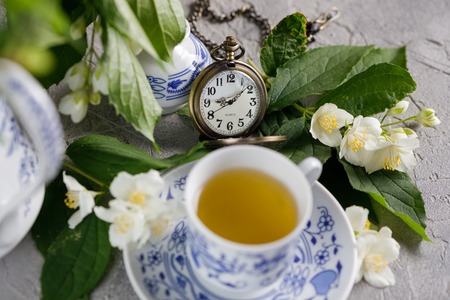 Blooming delicate jasmine flowers and a cup of tonic green tea decorated with a mechanical clock on a chain. Snow-white beautiful flowers. Close-up.の写真素材
