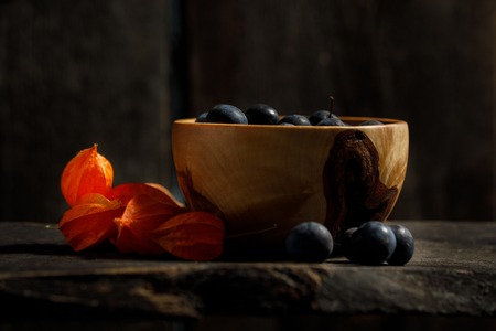 Autumn still life. Berries of plum in a wooden bowl. Ornament from berries of Physalis.の写真素材