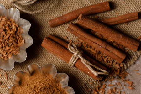 Cinnamon in baking tins and cinnamon sticks on a textured background with textiles under the burlap....