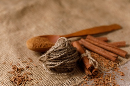 Fragrant sticks and a scattering of crushed cinnamon in a wooden spoon on the textile under the burlap. Top view.の写真素材