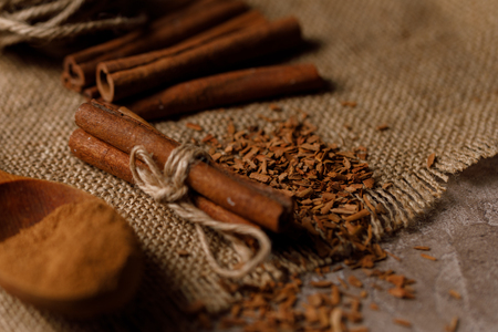 Shredded cinnamon in a wooden spoon and cinnamon sticks on a textured background with textiles under...