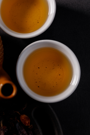 The process of brewing tea. Tea ceremony. Cups with a freshly brewed rosehip drink, dark mood. Close-up.の写真素材