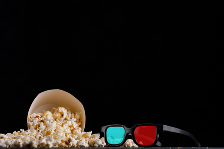 Snack for watching movies. A paper bucket with popcorn on a black background and 3 d glasses. Close-up.の写真素材