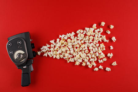 Retro movie camera with popcorn flying out of it on a red background. Cinema concept.の写真素材