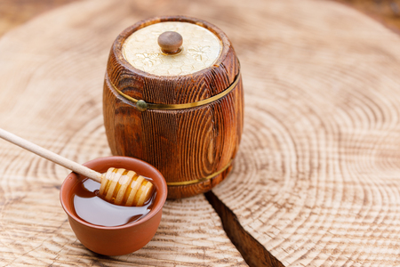 Wooden barrel with fresh honey and a honey spoon in a clay bowl on a wooden saw. Barrel. Close-up.の写真素材