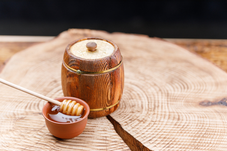 Wooden barrel with fresh honey and a honey spoon in a clay bowl on a textured wooden saw. Barrel. Close-up.の写真素材