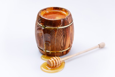 Fragrant fresh honey flowing from the barrel and honey stick in a drop of honey on a white...