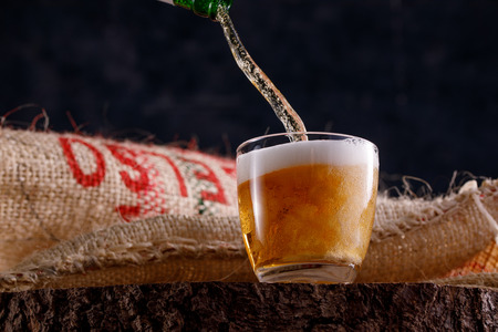 Light beer pours into a glass goblet standing on a wooden saw. Close-up.の写真素材