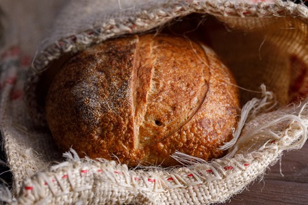 Traditional round artisan rye bread in a bag. Still life on wooden background. Close-up.の写真素材
