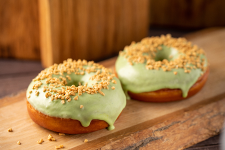 Concept of cooking, baking and food - close-up. Donuts with pistachio glaze and nut sprinkling on a decorative board. Trend colors. Appetizing still life.の写真素材