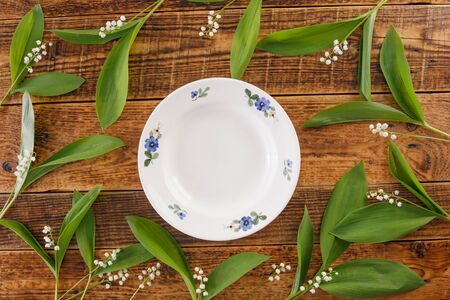 Plate and decor of lily of the valley flowers on the background of vintage wooden boards. Vintage background with flowers and place under the text. View from above. Flat lay. Cutlery. Vintage.の写真素材