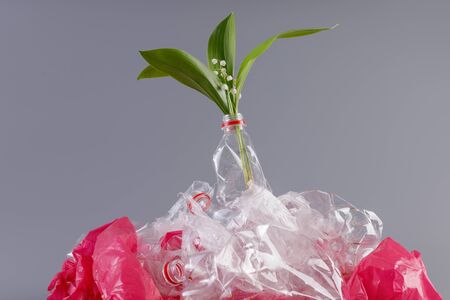 Gentle lily of the valley in a heap of plastic. Concept of environmental protection and plastic processing.の写真素材
