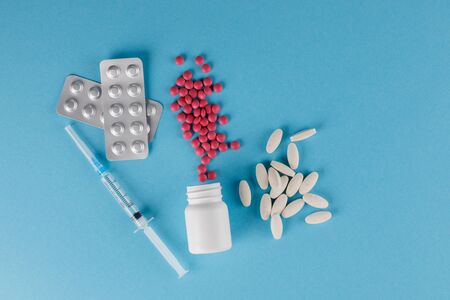Packing pills and medical syringe. A scattering of tablets. Pills spilling out of a jar on a blue background. Close-up.の写真素材