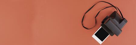 Instant photo frame and camera on a brown background. Concept of preservation of memories. Flat lay. Copy space. Banner.の写真素材